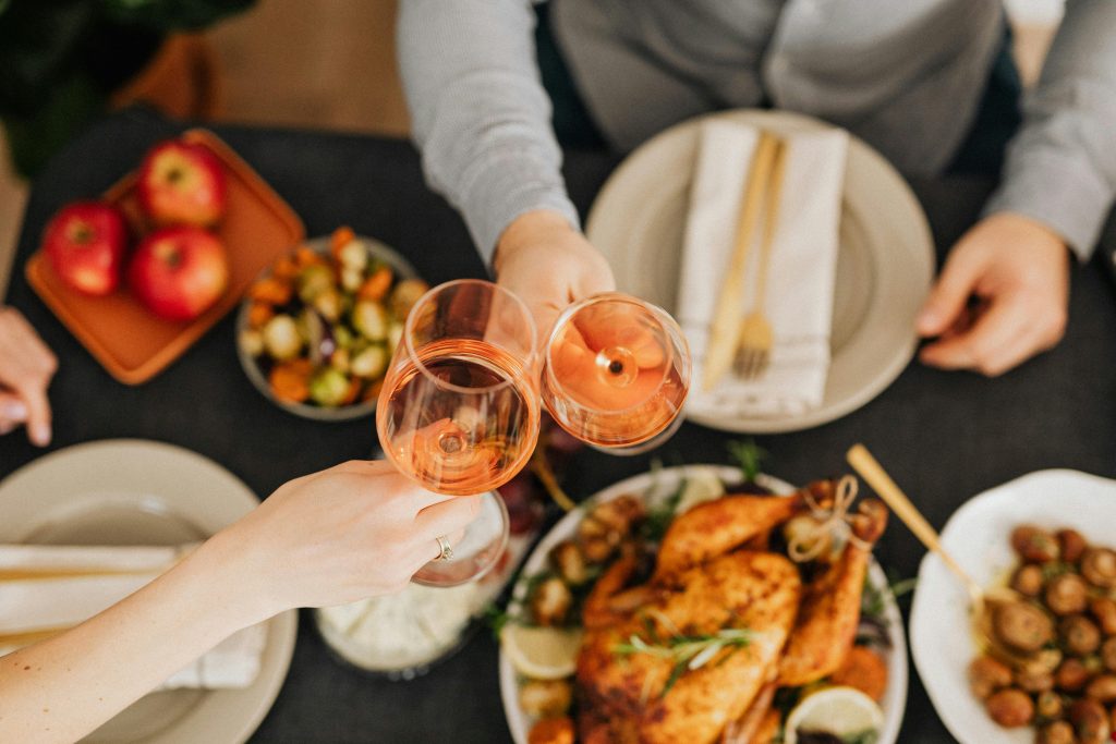 Christmas dinner. Roast chicken with veg on a table with 2 people raining glasses of wine