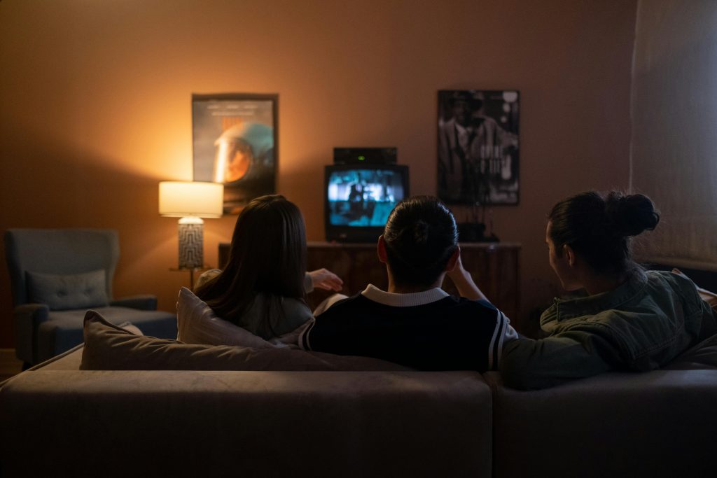 3 people sat on a sofa watching a movie